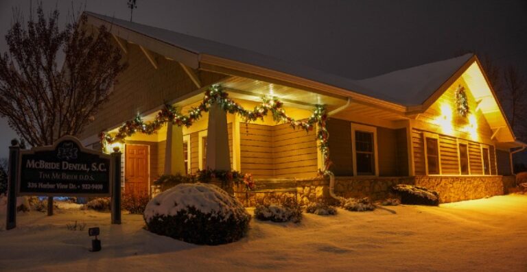 A night view of a building featuring lit wintery greenery and a wreath.
