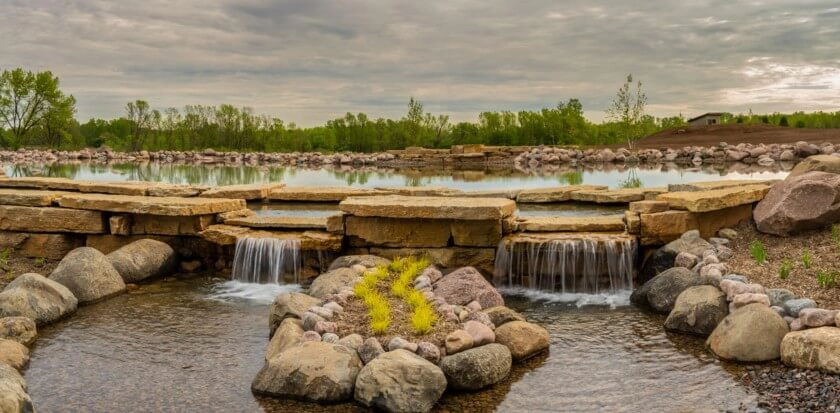 A wall that features two waterfalls separates a pond from another body of water on a lower level.